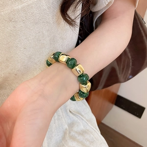 Detail of green crackle glass beads and gold metal spacers on a stretch bracelet