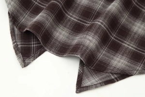 Close-up of the asymmetric hem and flannel texture on a brown plaid long sleeve shirt