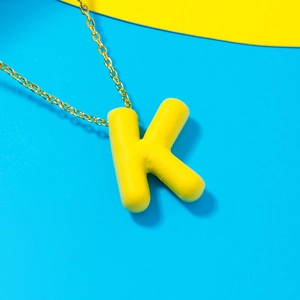 Minimalist gold-tone necklace with a bold yellow letter K pendant on a blue background