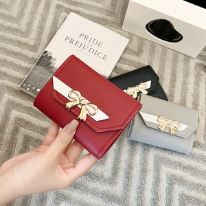 Detail of short tri-fold women's wallet featuring a gold bow buckle and contrasting edge
