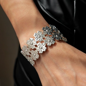 Detail of silver layered floral bangle with metallic finish on model wrist with black leather