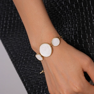 Gros plan d'un bracelet doré avec cercles en émail blanc porté sur poignet avec cuir