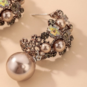Detailed close-up of C-shaped floral earrings with champagne pearls and dark rhinestones