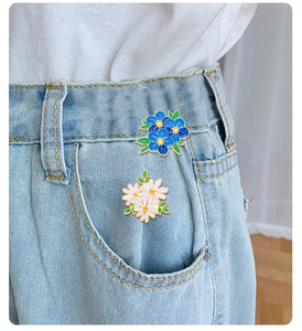 Detailed view of blue floral and white daisy enamel pins pinned to denim jeans pocket