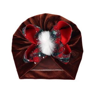 Detail of baby velvet turban featuring a red plaid bow and white plush pompom