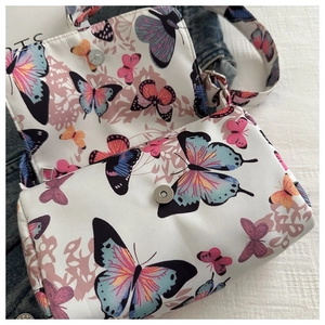 Close-up of white crossbody bag with butterfly prints and silver magnetic snap closure