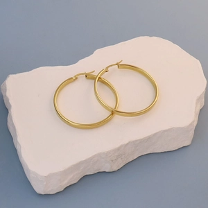 Detailed view of large gold hoop earrings with polished finish on decorative white stone