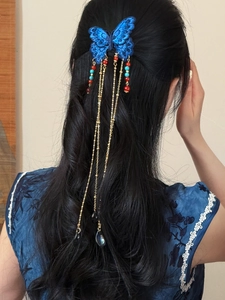 Détail de la pince à cheveux papillon bleu avec gland doré sur cheveux noirs bouclés
