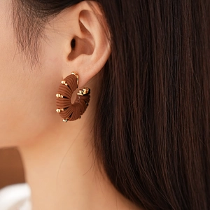 Close-up of model wearing C-shaped brown cord wrapped earrings with golden metal beads