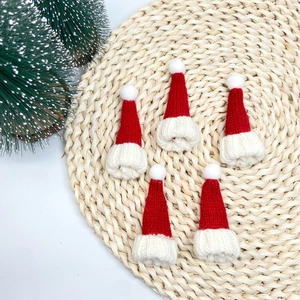 Cinq mini bonnets de Noël tricotés rouge et blanc pour poupées sur un tapis beige tressé
