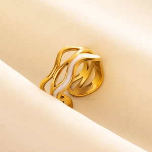 Macro shot of gold wave ring with white enamel detail on a soft beige fabric background