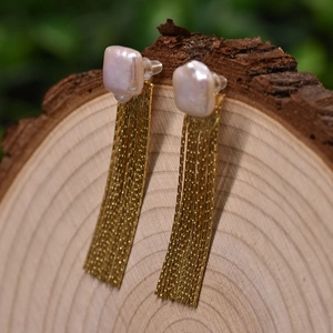 Elegant baroque pearl drop earrings with long gold tassel chains on wooden base