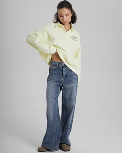 Detail of light yellow polo collar sweatshirt with SOHOHOUS embroidery and blue jeans