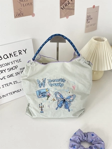 Close-up of butterfly embroidery and Butterfly Poetry lettering on green oxford tote bag