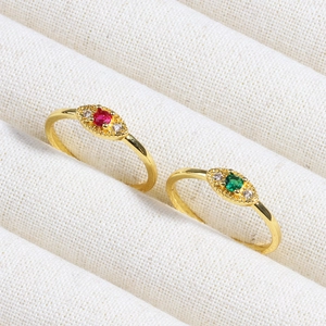 Detailed shot of gold eye-shaped rings with red and emerald green zircon stones