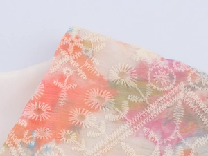 Détail macro de broderie florale blanche sur une robe dégradée rose et orange