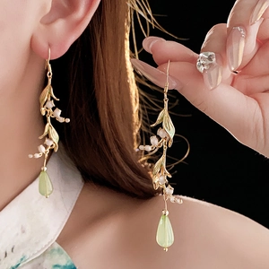 Close-up of elegant lily of the valley earrings with white buds and green teardrop charm