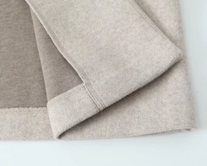 Gros plan du tissu de manteau en laine avoine montrant la texture douce et l'ourlet
