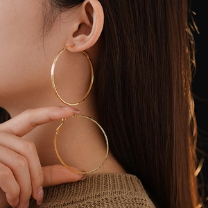 Detailed close-up of a model wearing large textured gold-plated hoop earrings