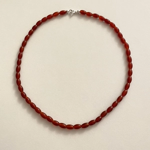 Minimalist oval red agate bead necklace with a silver spring clasp on beige background