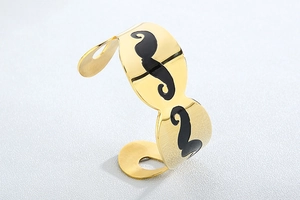 Detailed view of polished gold-plated cuff bracelet featuring a black enamel mustache pattern