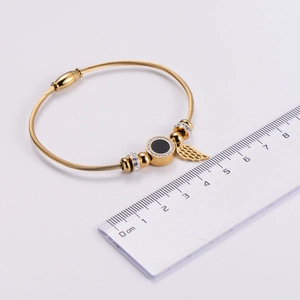 Close-up of gold wire bangle with angel wing charm and crystal disc next to ruler