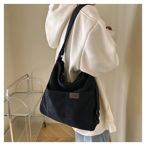 Détail du sac bandoulière en velours côtelé noir avec écusson en cuir et sangle