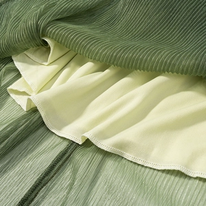 Close-up of green pleated fabric texture with fine stitching and soft yellow inner lining