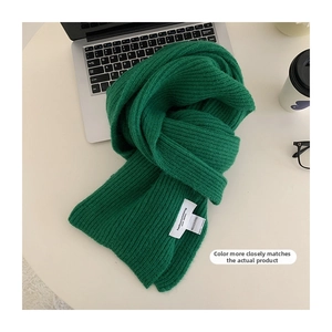 Close-up of thick green knitted scarf with ribbed texture on a white workspace desk