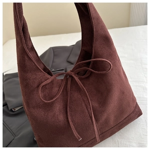 Close-up of brown suede shoulder bag featuring a decorative bow on a soft white fabric