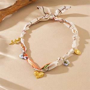 Detailed shot of a printed silk scarf necklace with golden heart and floral charms