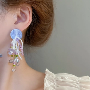 Detail view of long tassel earrings with light blue marble resin and purple resin flowers