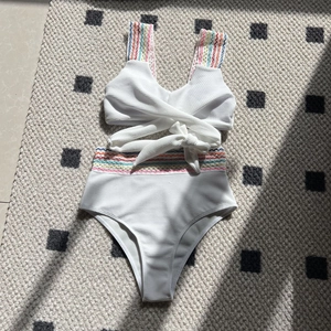 Macro detail of white high-waisted bikini with colorful wavy embroidered rainbow straps