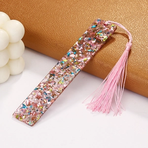 Macro detail of a clear acrylic bookmark with colorful foil flakes and a pink tassel