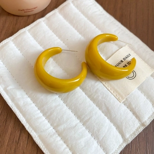 Vue détaillée de créoles en forme de C en résine jaune sur un tissu blanc texturé