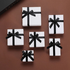 Elegant white jewelry boxes with black ribbon bows in various sizes on brown background
