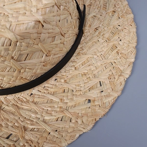 Detailed macro view of woven raffia texture and slim black leather band on straw hat