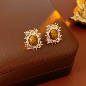 Macro shot of tiger eye stone earrings with gold woven texture on brown leather box