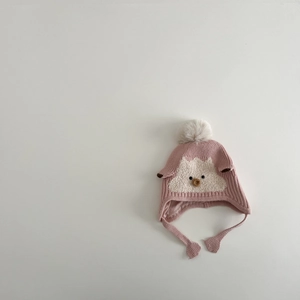 Detail of pink knitted baby earflap hat featuring a plush animal face and fuzzy pom-pom