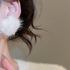 Close-up of white plush pom-pom earring on model with soft mink fur texture detail