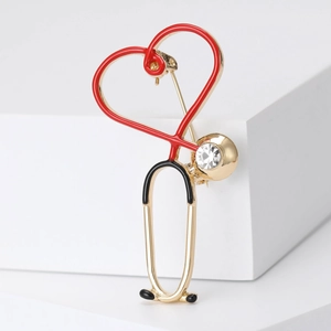 Golden stethoscope brooch with red heart and rhinestone accent on white background