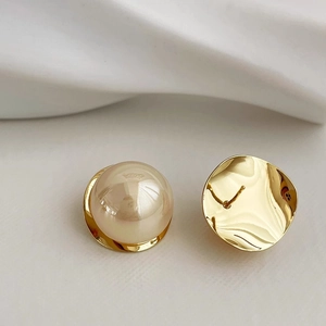 Elegant gold metal stud earrings with large round cream pearls on white fabric