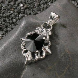 Close-up of vintage steel cross pendant with black gemstone on dark natural stone