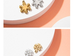 Macro shot of gold and silver snowflake charms on a pedestal with a soft pink backdrop