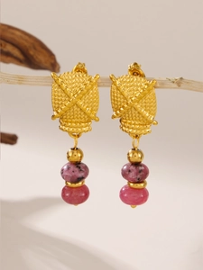 Detail of vintage gold textured earrings with pink beads hanging on a wooden branch