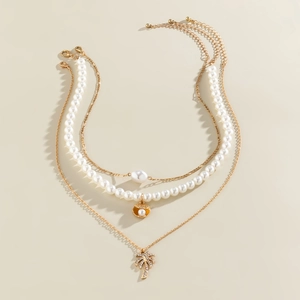 Detail of gold layered necklace with baroque pearls and palm tree charm on beige background