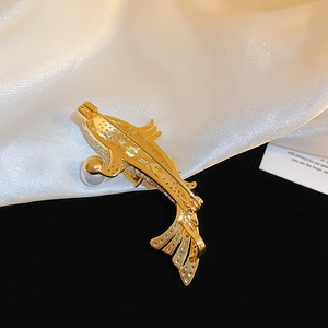 Macro shot of gold-plated fish brooch with hollow metalwork and pearl accents