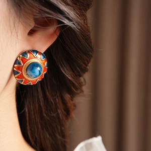 Close-up of vintage round enamel earrings with red, blue, and gold sunburst details