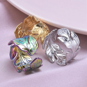 Detailed close-up of leaf-shaped rings in gold, silver and rainbow on pink fabric