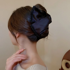Detail of a black satin bow hair claw clip with beads on a woman's hair in a low bun